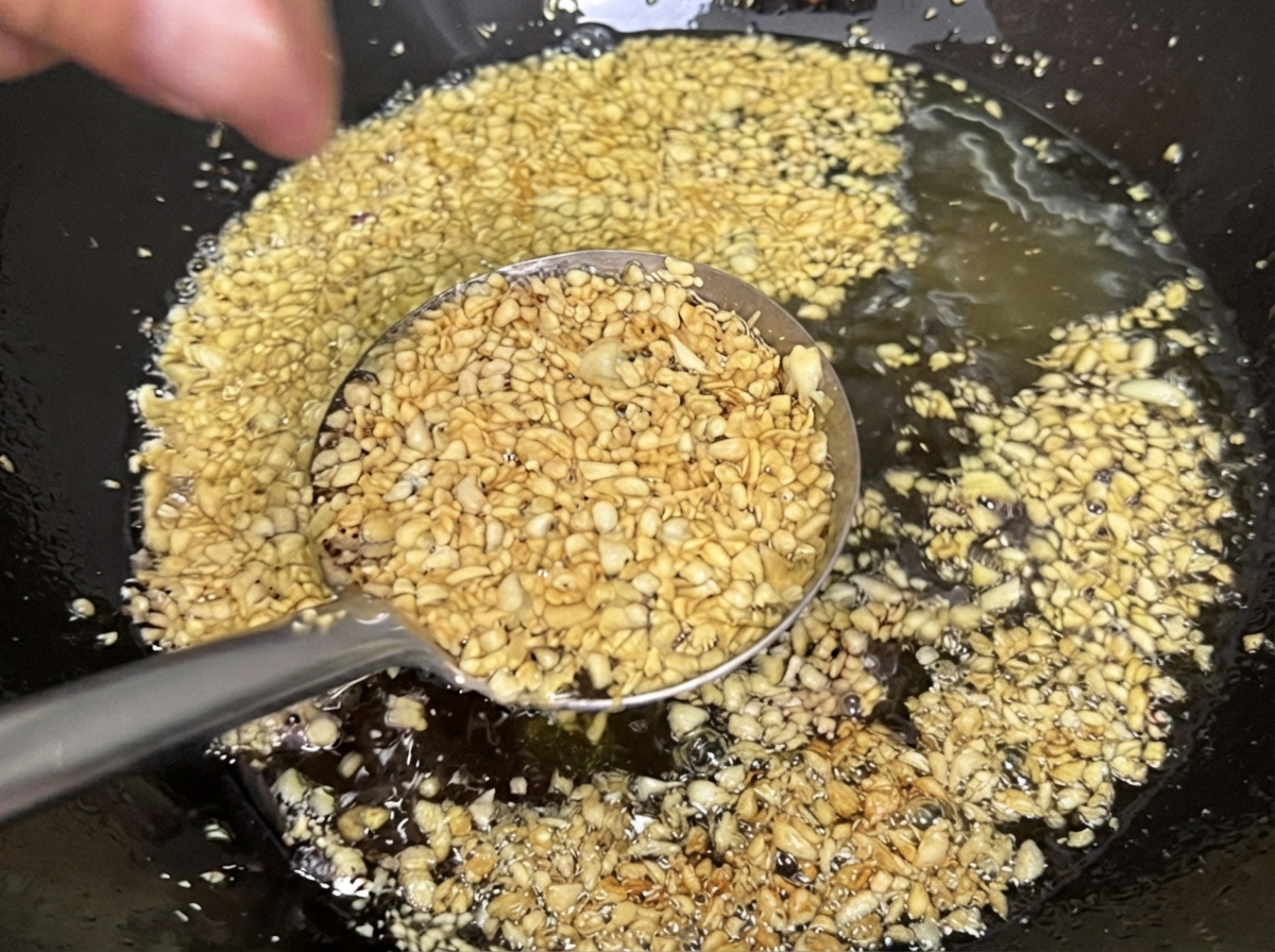 Ajo picado friéndose en aceite dentro de un wok, tomando un color amarillo dorado claro y crujiente.