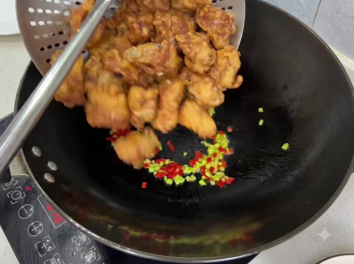 Costillas de cerdo fritas, doradas y crujientes siendo vertidas desde un colador a un wok con chiles.
