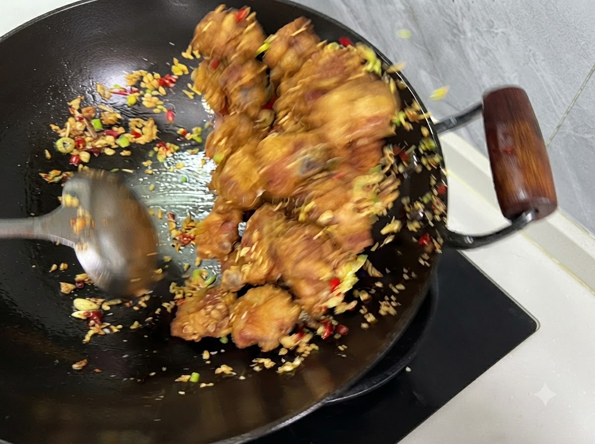 Costillas, chiles y ajo siendo mezclados con un cucharón dentro de un wok.