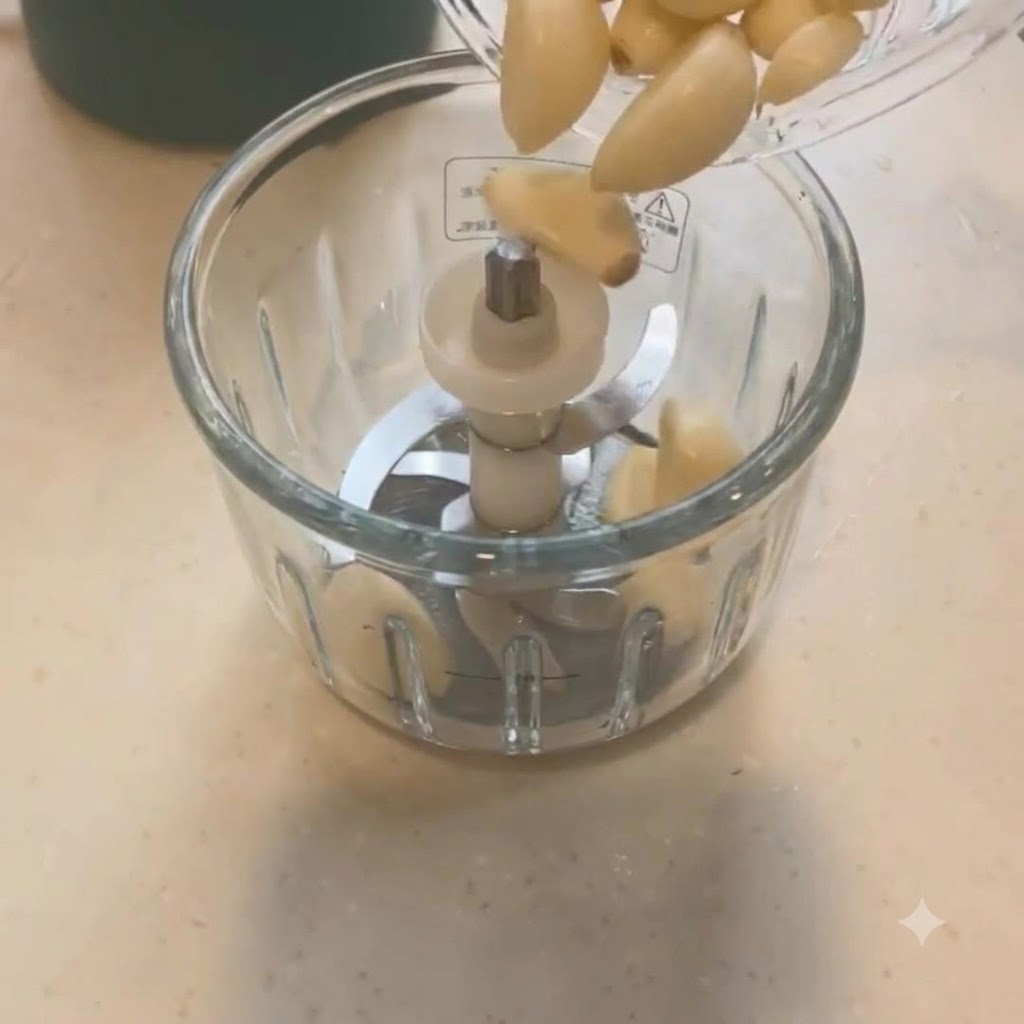 Dientes de ajo siendo vertidos en una picadora mini con cuchillas.