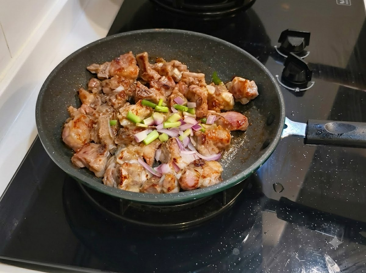 Cebollinos picados y jengibre esparcidos sobre las costillas de cerdo en la sartén.