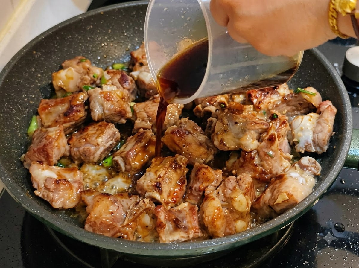 Salsa oscura siendo vertida desde una taza medidora en la sartén con costillas de cerdo.