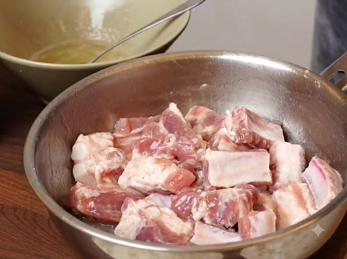 Trozos de costilla de cerdo reposando en un tazón de metal con los condimentos y almidones añadidos antes de mezclar.
