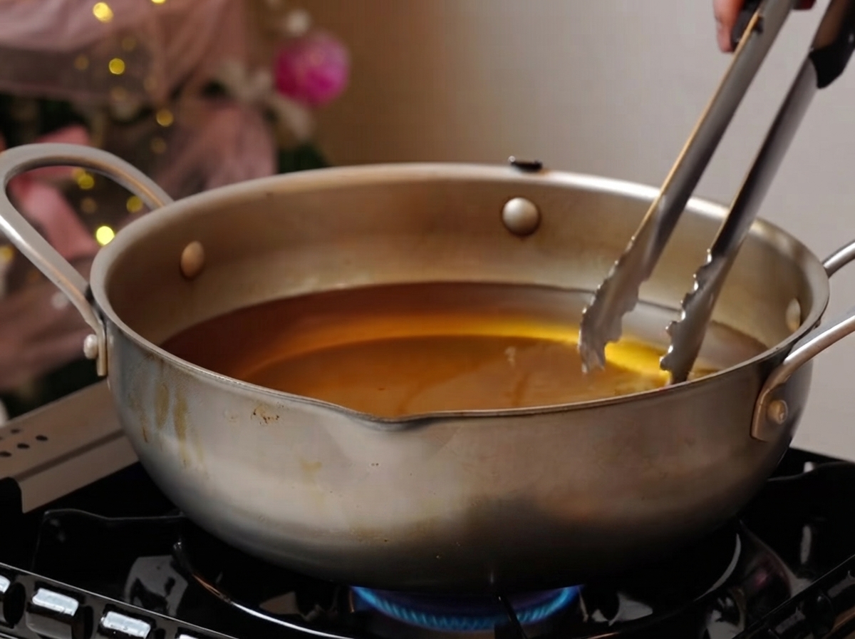 Costillas de cerdo friéndose suavemente en una olla ancha con aceite sobre una hornalla.