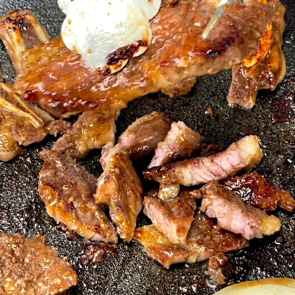 Pinzas sosteniendo una costilla corta cocida mientras las tijeras la cortan en porciones más pequeñas sobre una sartén caliente.