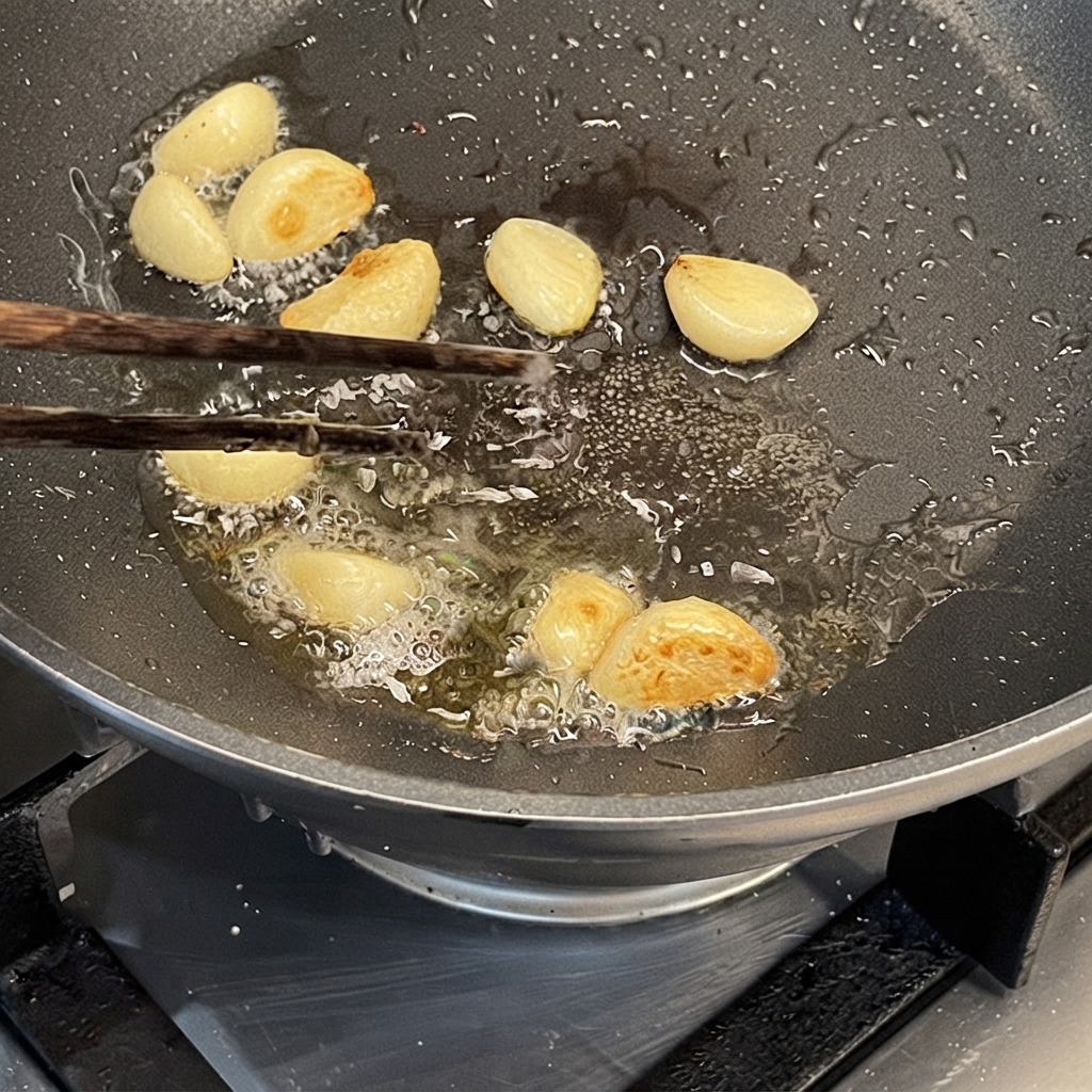 Dientes de ajo salteándose en aceite en una sartén caliente usando palillos.