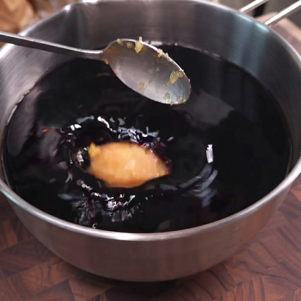 Una cucharada de ajo picado siendo depositada en una olla de adobo de salsa de soya oscura.