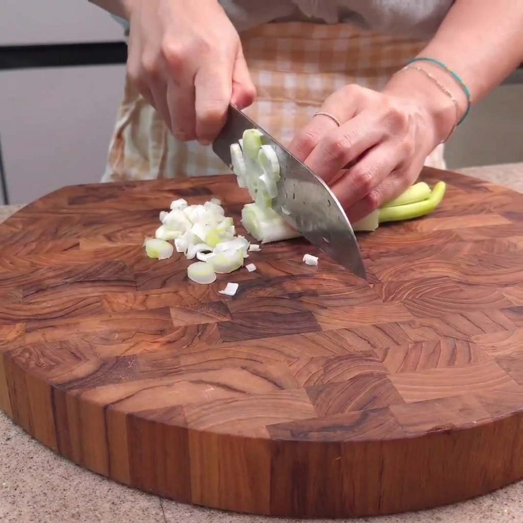 Cebollinos siendo picados sobre una tabla de cortar de madera con un cuchillo de chef.