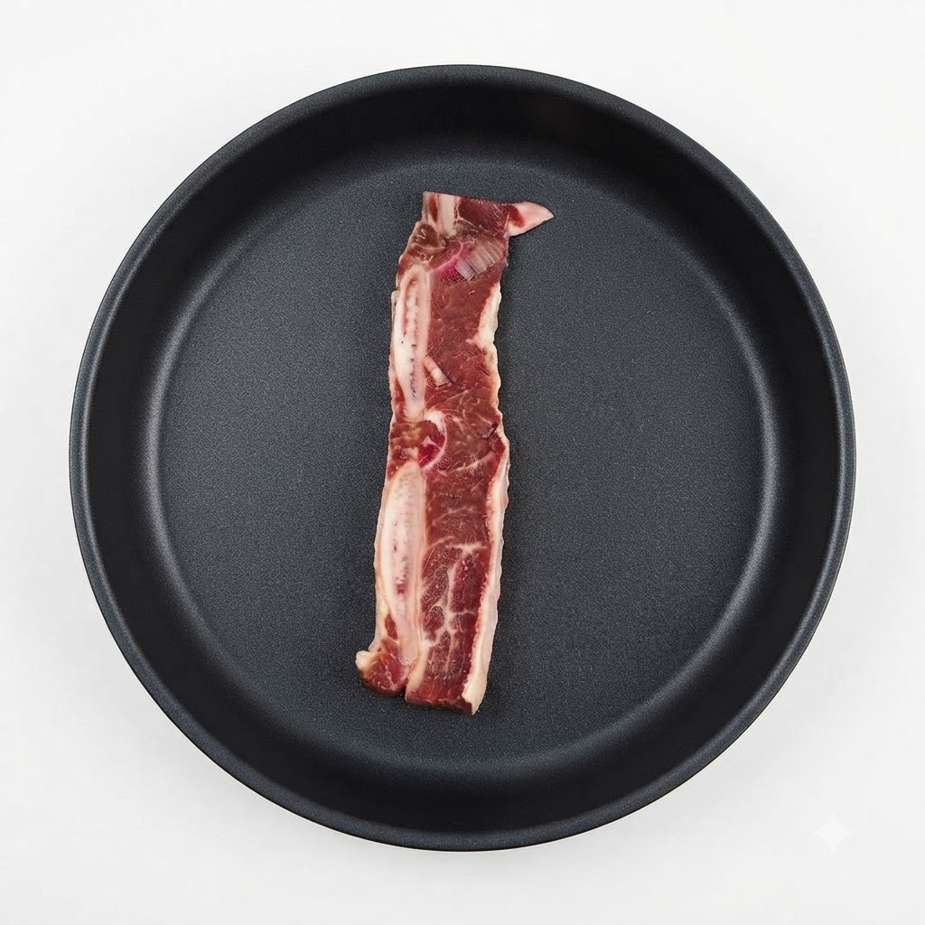 Una sola pieza de costilla de res marinada colocada dentro de una sartén oscura.