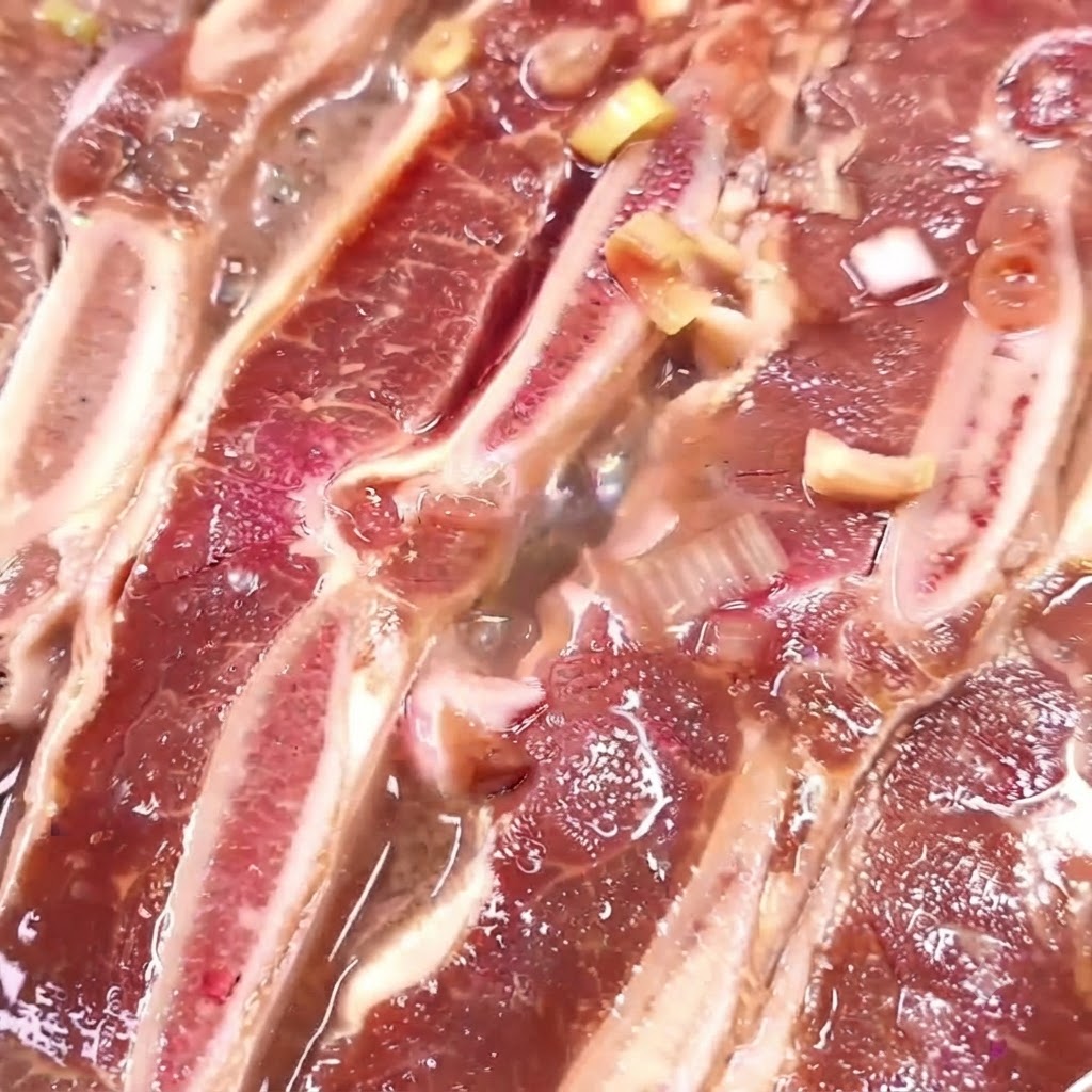 Costillas de res cocinándose en una sartén con marinada hirviendo y reduciéndose.