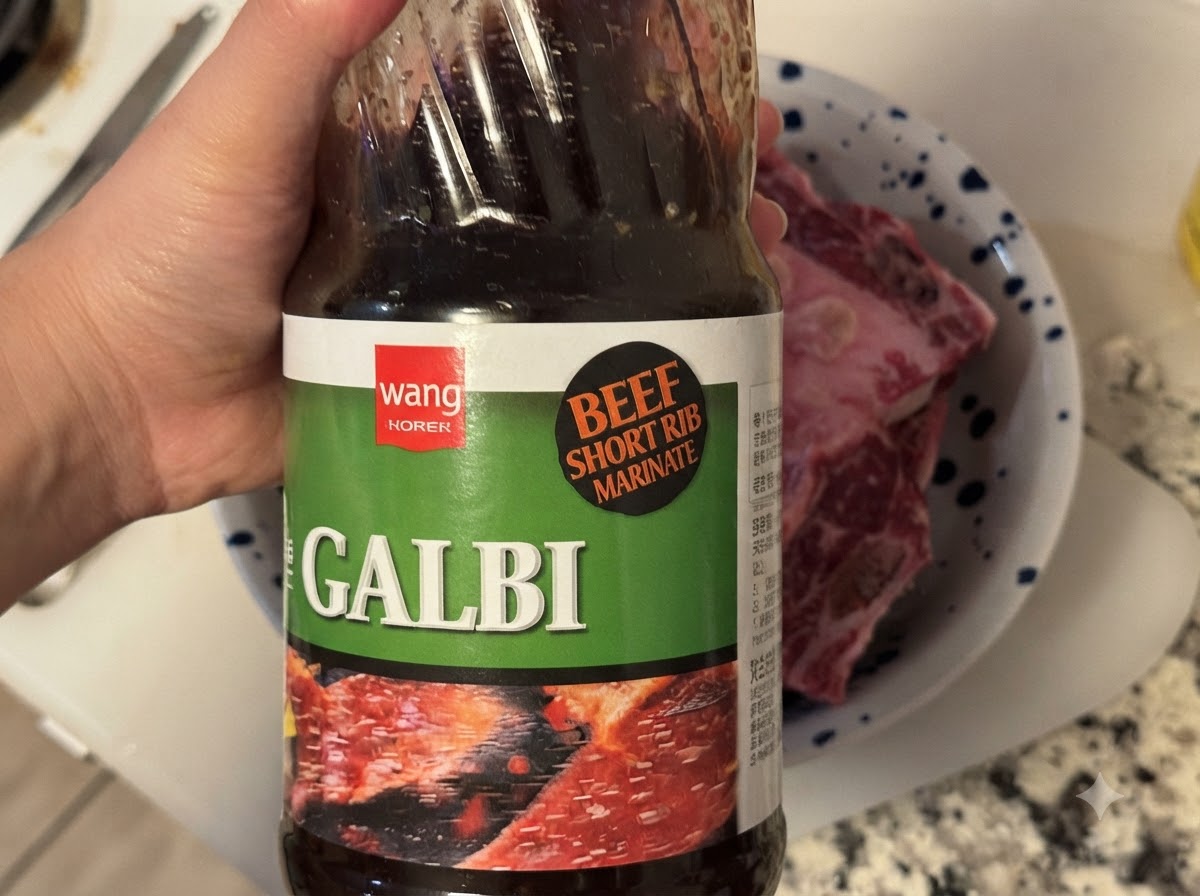 Una botella de salsa coreana barbacoa Galbi siendo vertida en un tazón que contiene costillas de res crudas.