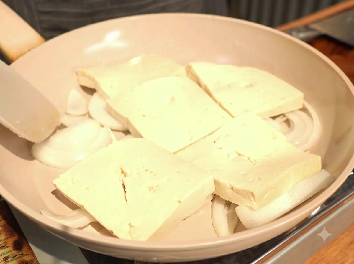 Disponiendo las rebanadas gruesas de tofu en una sola capa ligeramente superpuesta sobre las cebollas.