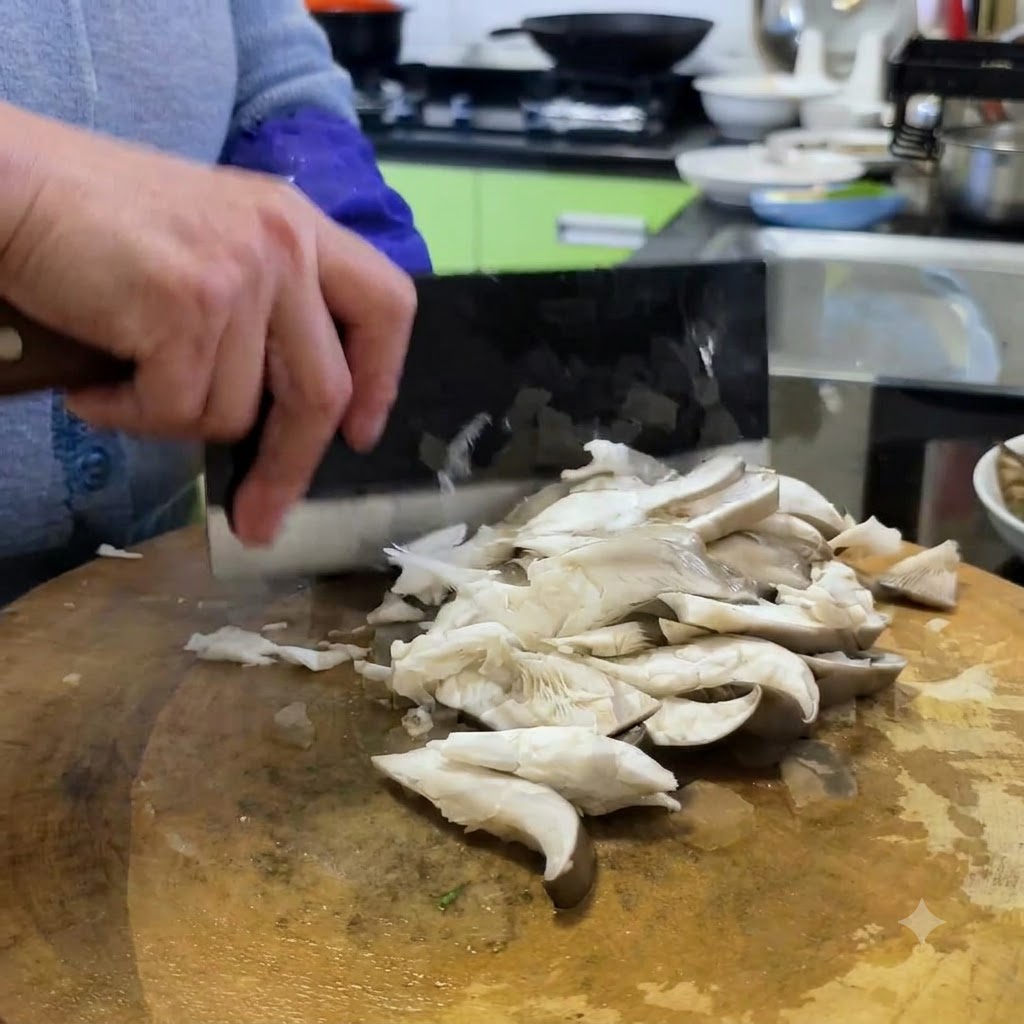 Setas ostra siendo cortadas en porciones más pequeñas sobre una tabla de cortar de madera usando un cuchillo de carnicero.