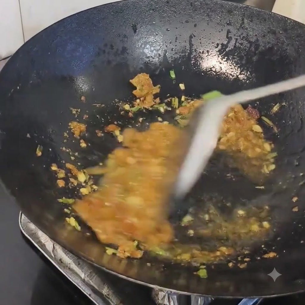 Residuo de manteca de cerdo siendo mezclado con los aromáticos salteados en un wok caliente.