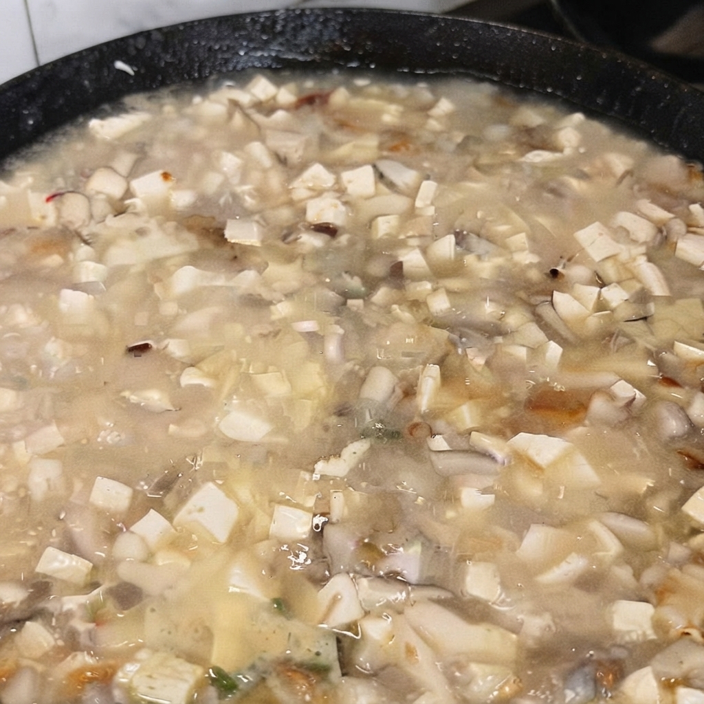 Una cucharada de glutamato monosódico siendo añadida a la sopa de tofú hirviendo.