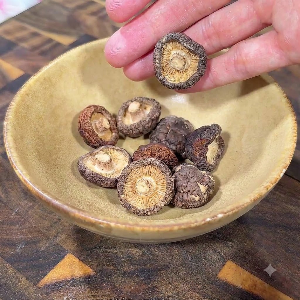 Setas shiitake deshidratadas reposando dentro de un tazón de cerámica amarillo sobre una superficie de madera.