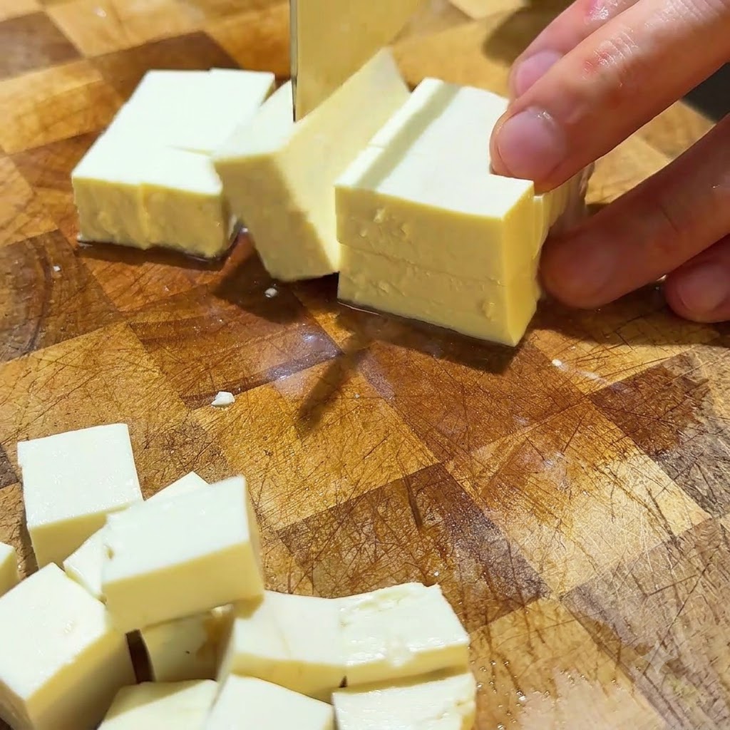 Tofu sedoso siendo cortado en pequeños cubos ordenados sobre una superficie de corte de madera.