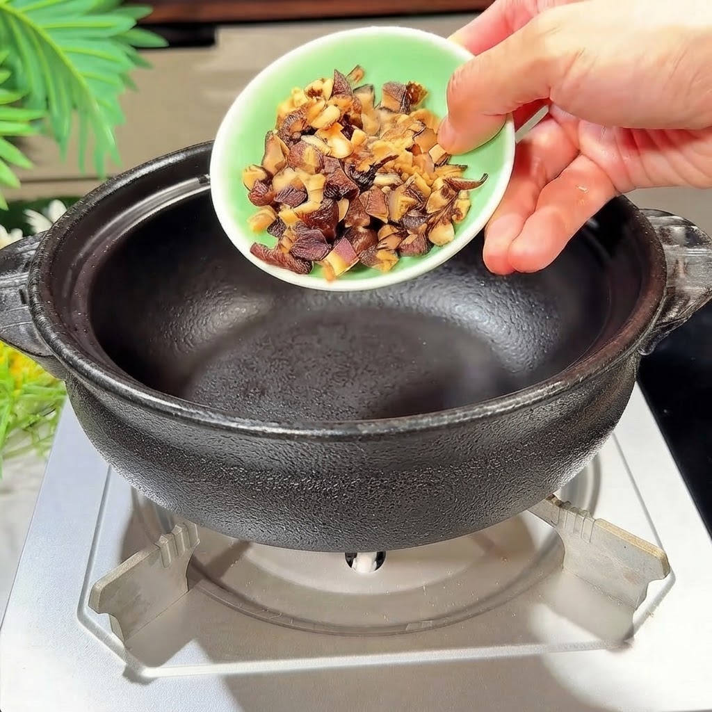 Setas shiitake en cubos siendo vertidas en una olla de barro negra calentada.