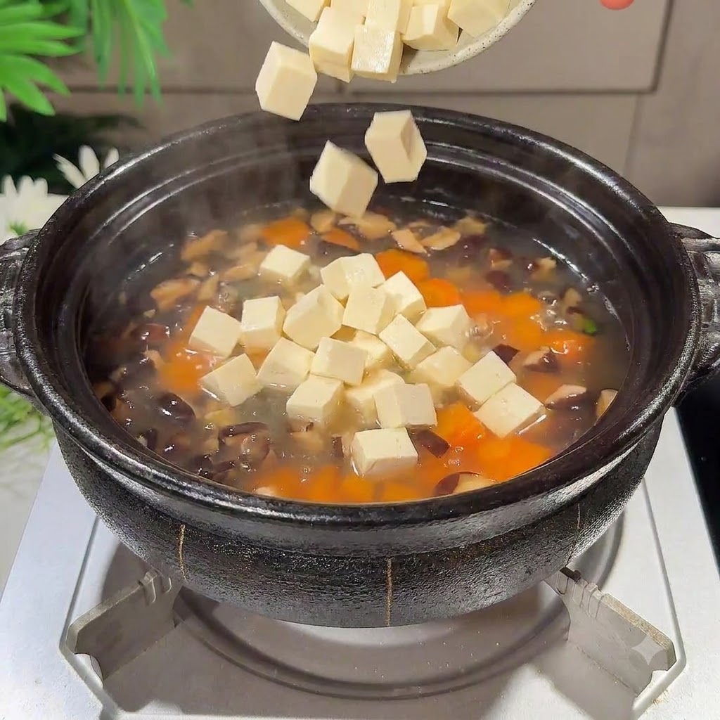 Trozos de tofu sedoso en cubos cayendo en la olla de sopa a fuego lento.