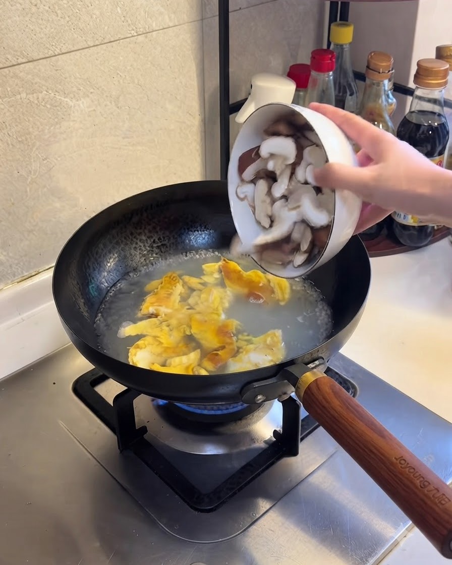Champiñones shiitake en rodajas siendo añadidos a la mezcla de agua hirviendo y huevo.