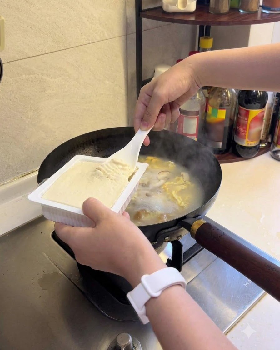 Tofú blando siendo añadido a la sopa a fuego lento.