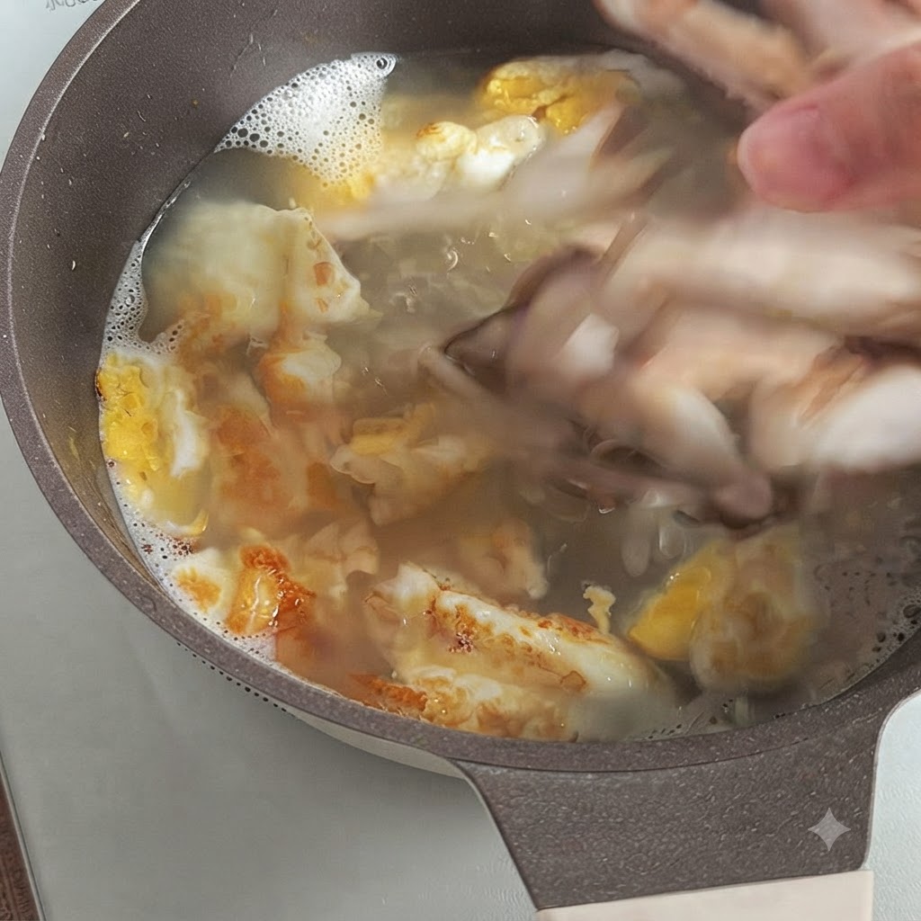 Una mano dejando caer champiñones shiitake frescos en rodajas en un caldo hirviendo con trozos de huevo frito.
