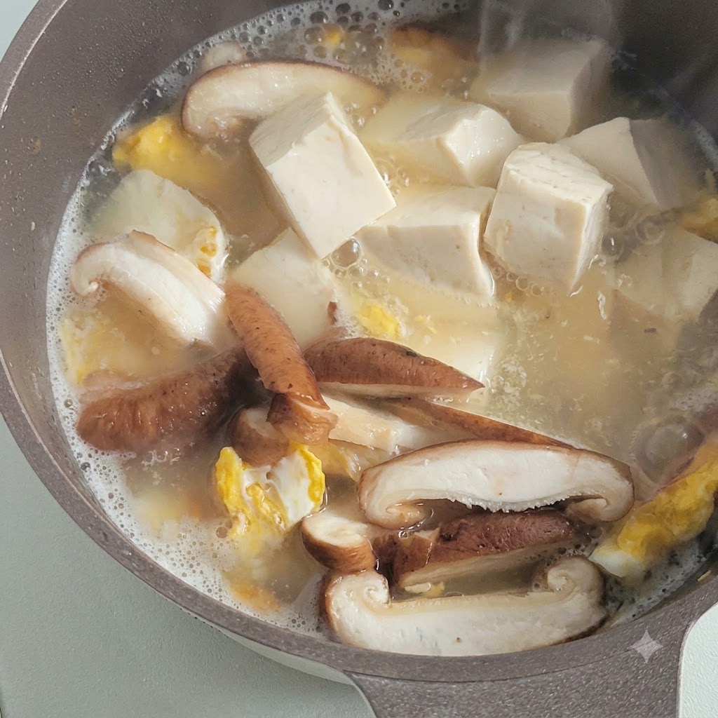 Cubos de tofu blanco suave hirviendo a fuego lento en un caldo sabroso junto con champiñones en rodajas y trozos de huevo frito.