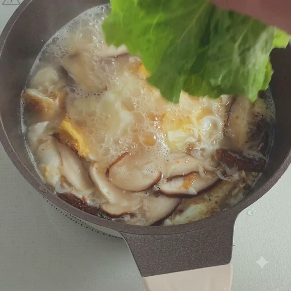 Hojas de lechuga fresca cayendo en una olla de sopa burbujeante con champiñones y huevos.