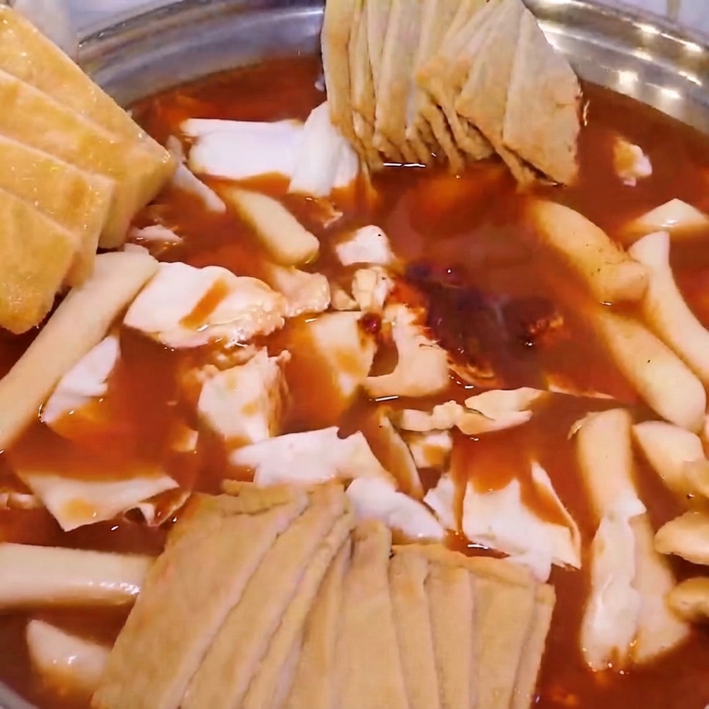 Un hot pot armado con repollo, pasteles de arroz, pasteles de pescado, cubierto con tofu frito y cebollas verdes.
