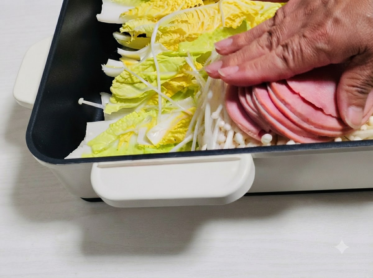 Rodajas de jamón y otros ingredientes dispuestos sobre las verduras en la olla.