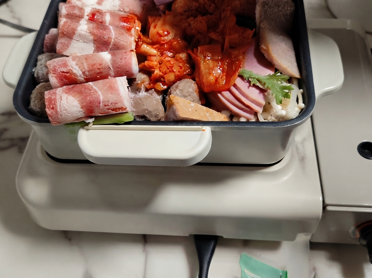 Una olla caliente llena de capas organizadas de carne, verduras y pasteles de arroz con caldo vertido sobre ellos.