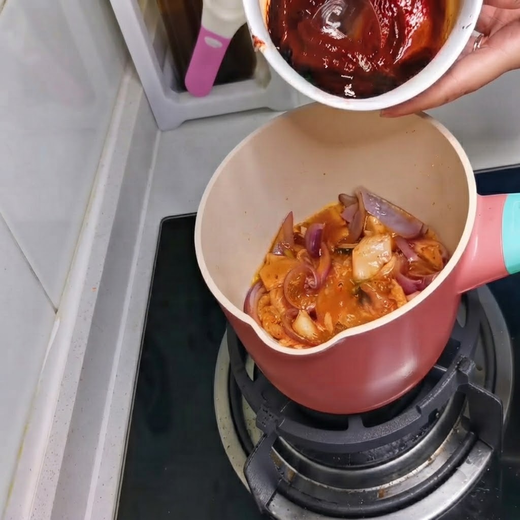 Un tazón que contiene una mezcla de salsa de color rojo oscuro siendo vertida en la olla.