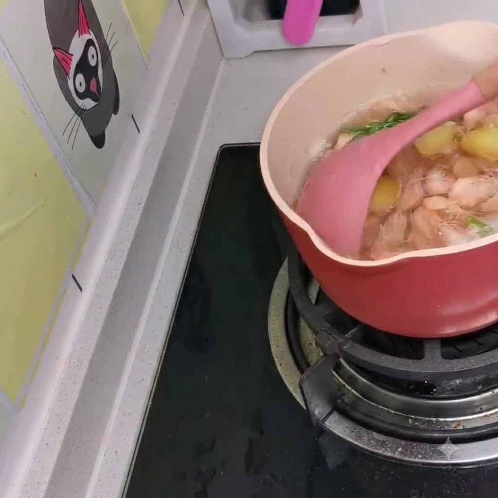 Camarones blancos pequeños siendo revueltos en una olla a fuego lento de ramen al estilo coreano usando una espátula rosa.
