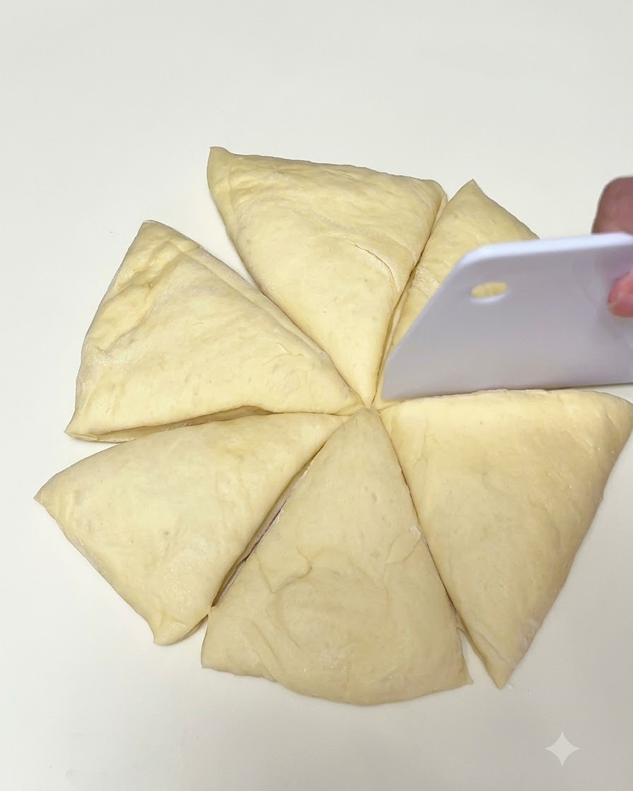 Masa cortada en seis porciones triangulares sobre una superficie blanca con un raspador de masa blanco.