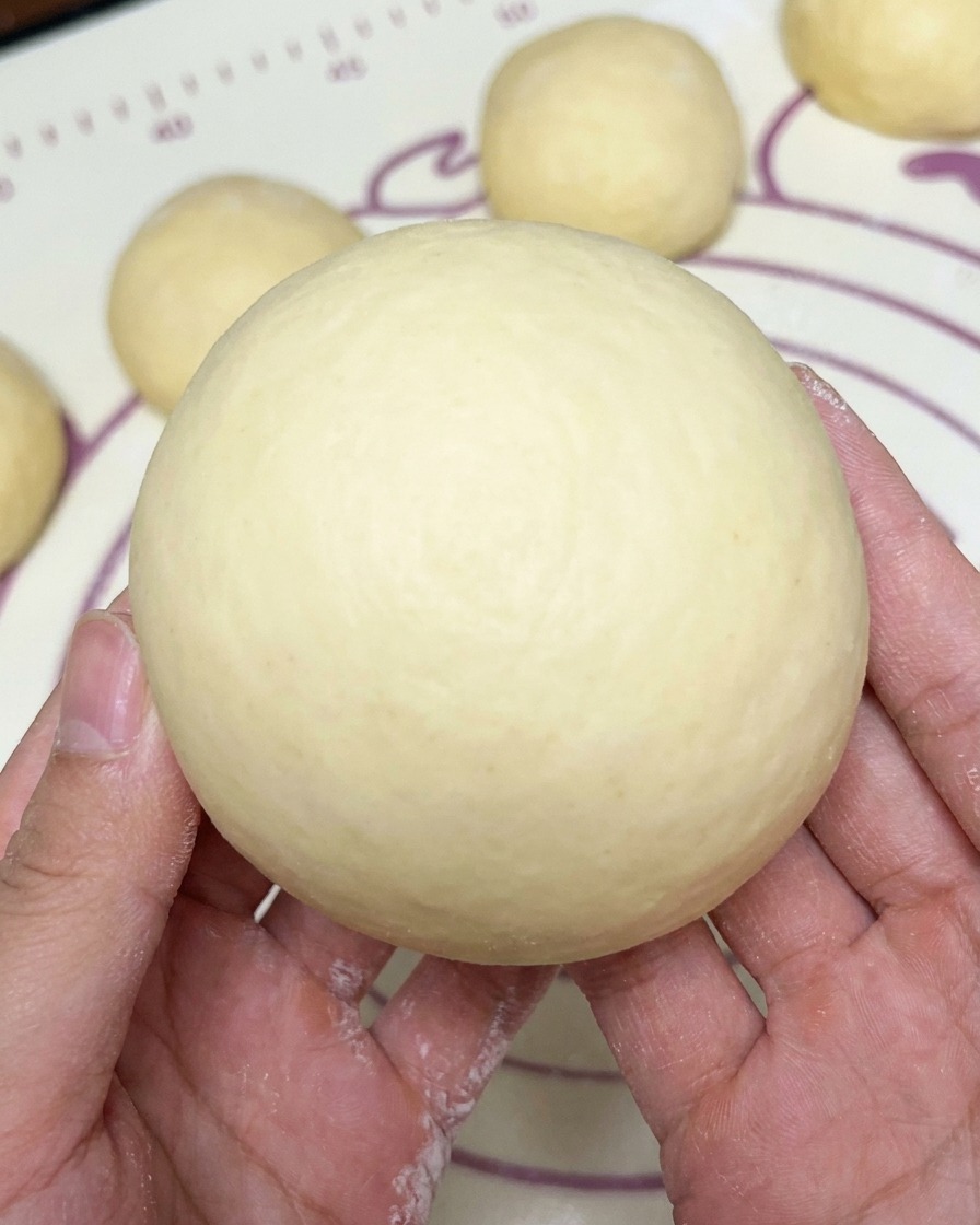 Una bola de masa redonda y suave sostenida en ambas manos, con otras bolas formadas en el fondo.