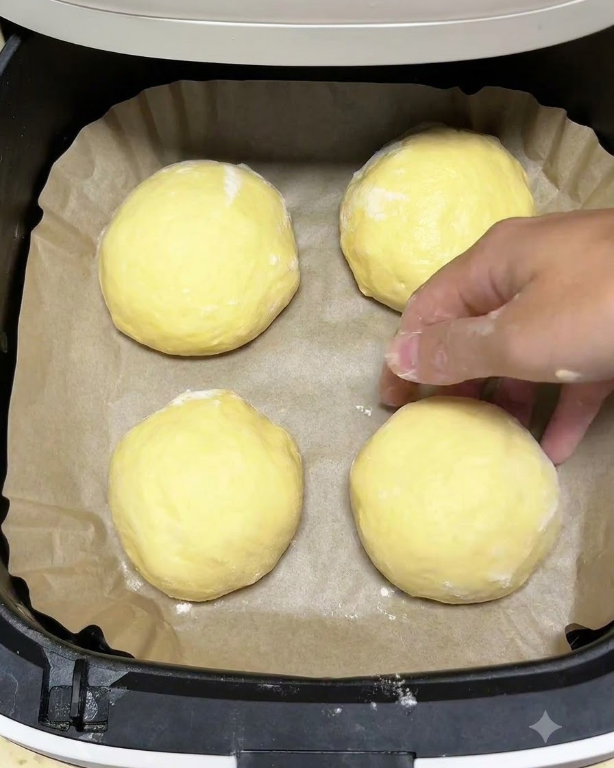 Cuatro bolas de masa redondas dispuestas dentro de una canasta de freidora de aire forrada con papel pergamino marrón.