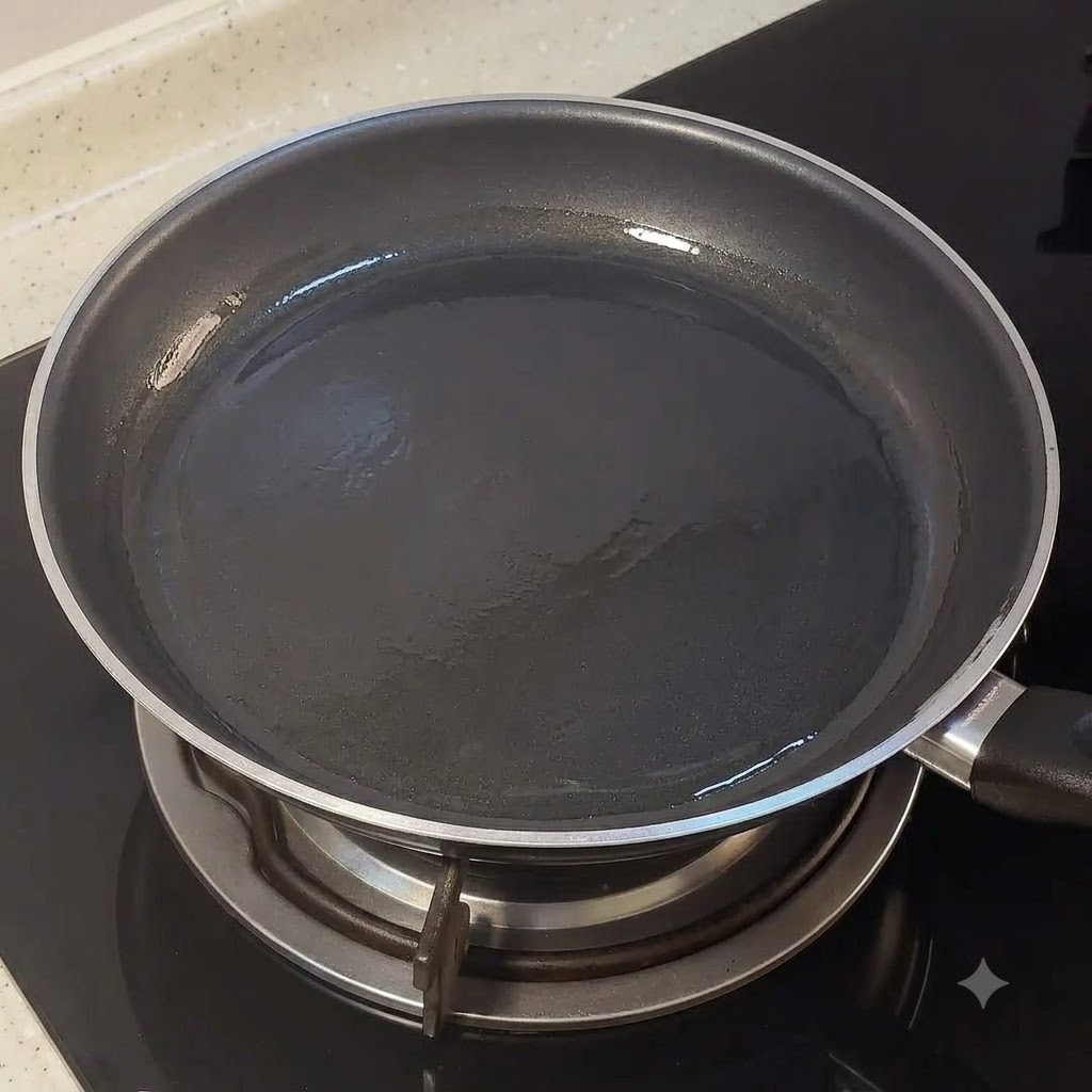 Una sartén negra vacía sobre el quemador de una estufa con una ligera capa de aceite.