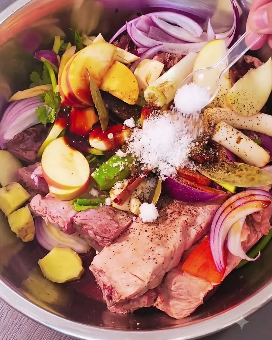Manos con guantes mezclando costillas de cerdo y aromáticos en un bol metálico.