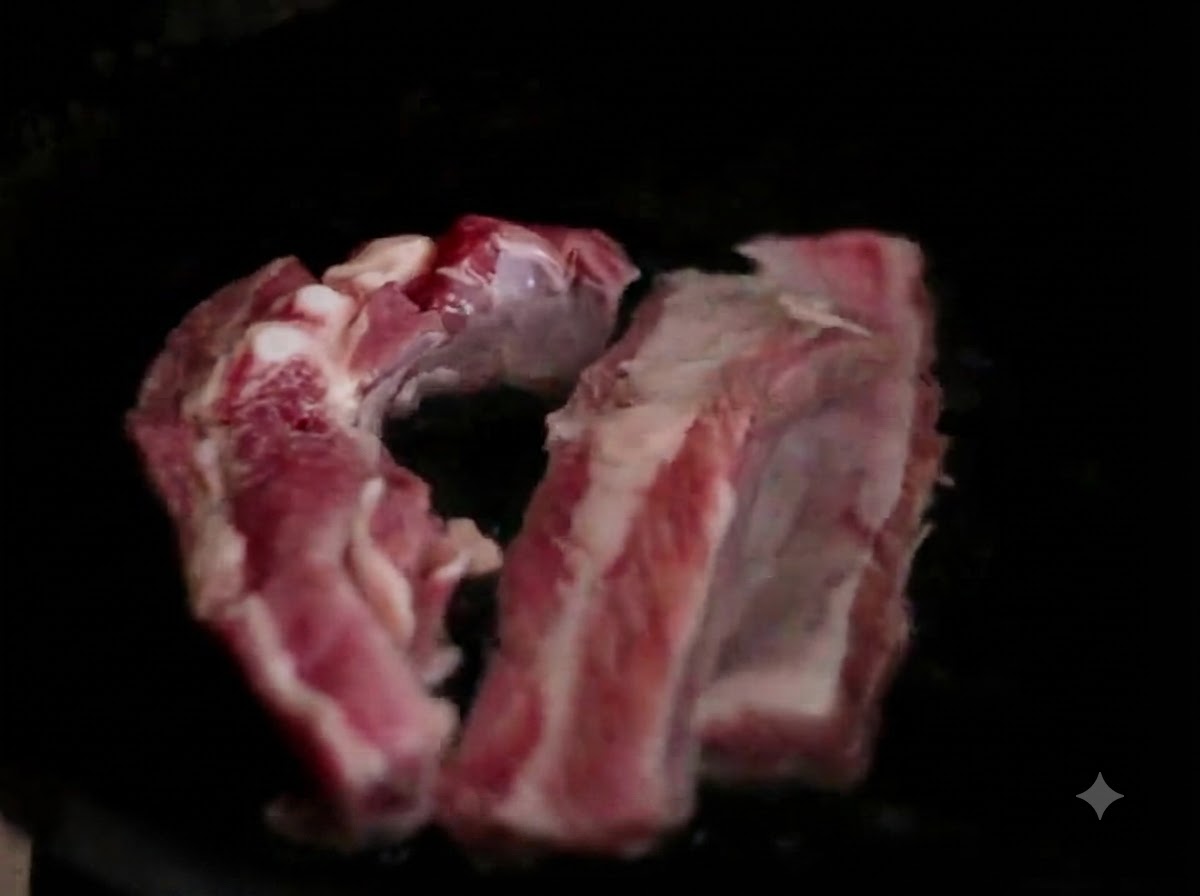 Tiras de costillas de cerdo crudas dentro de una olla oscura.