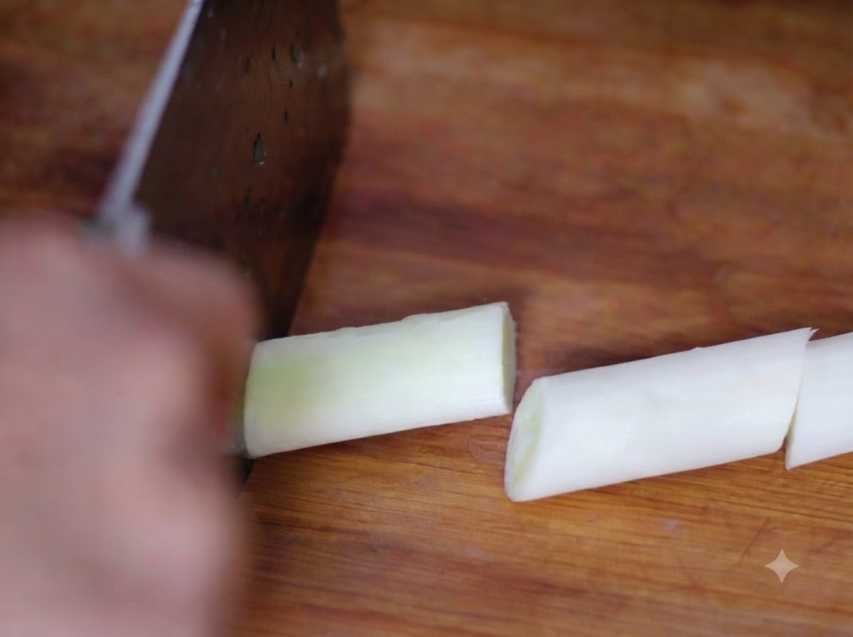 Un cuchillo cortando secciones de cebollín fresco en una tabla de madera.