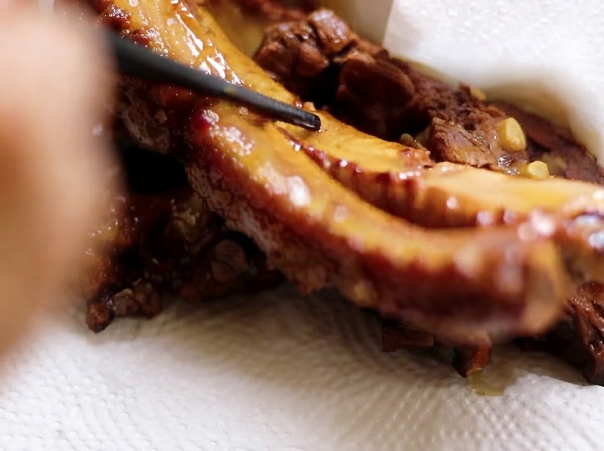Costillas de cerdo levantadas con palillos negros y reposando sobre papel absorbente blanco.