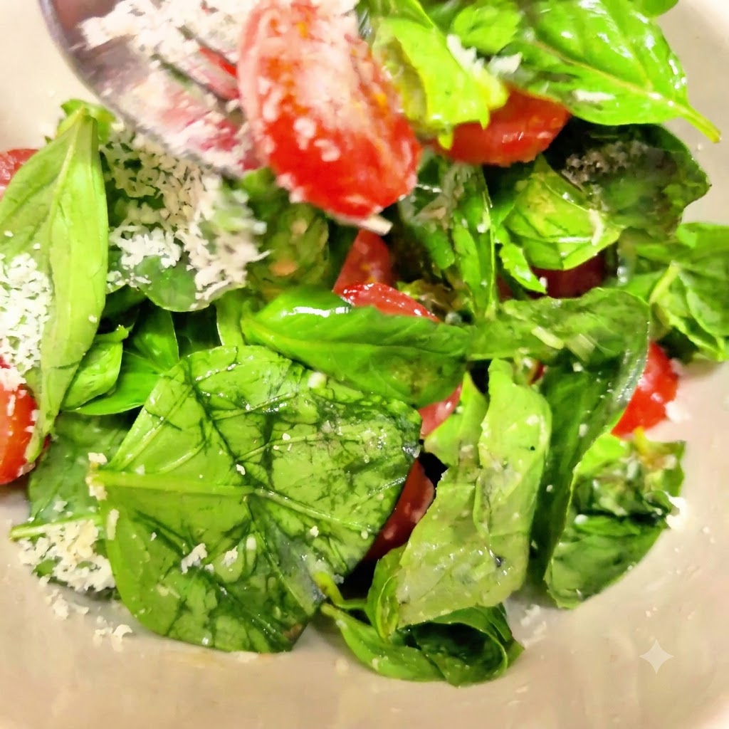 Hojas de albahaca fresca y tomates cherry partidos mezclándose con queso parmesano rallado usando un tenedor de metal en un bol blanco.