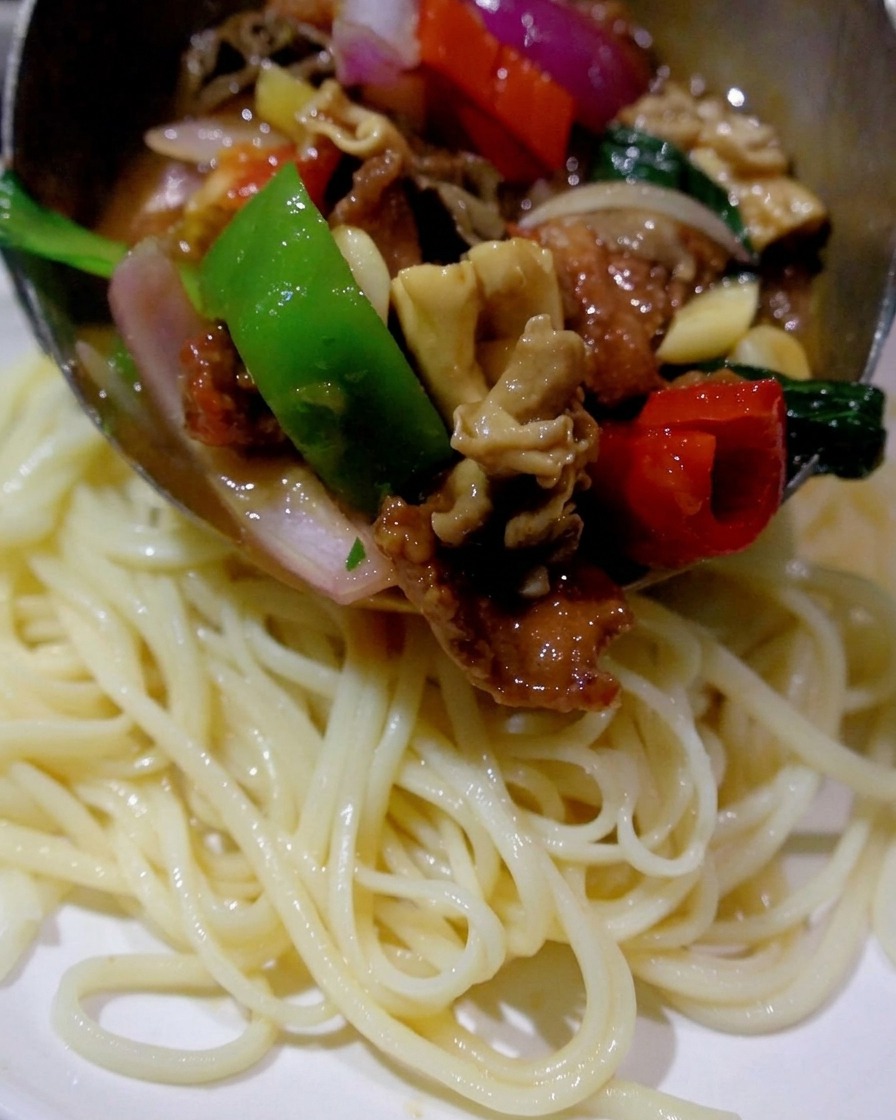 Un cucharón vertiendo la mezcla caliente de setas, carne y pimientos sobre un plato de fideos blancos cocidos.