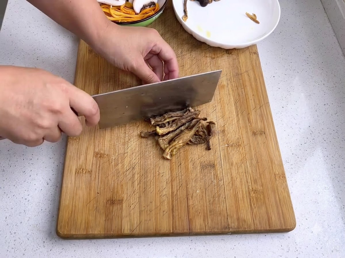 Hongo de bambú remojado siendo cortado en trozos más pequeños con un cuchillo sobre una tabla de madera.