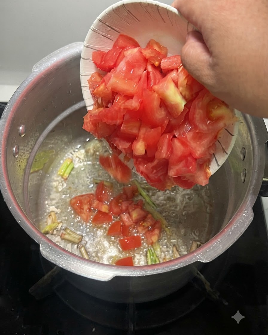 Tomates rojos cortados en dados siendo vertidos desde un tazón de papel en una olla de metal con aromáticos burbujeantes.