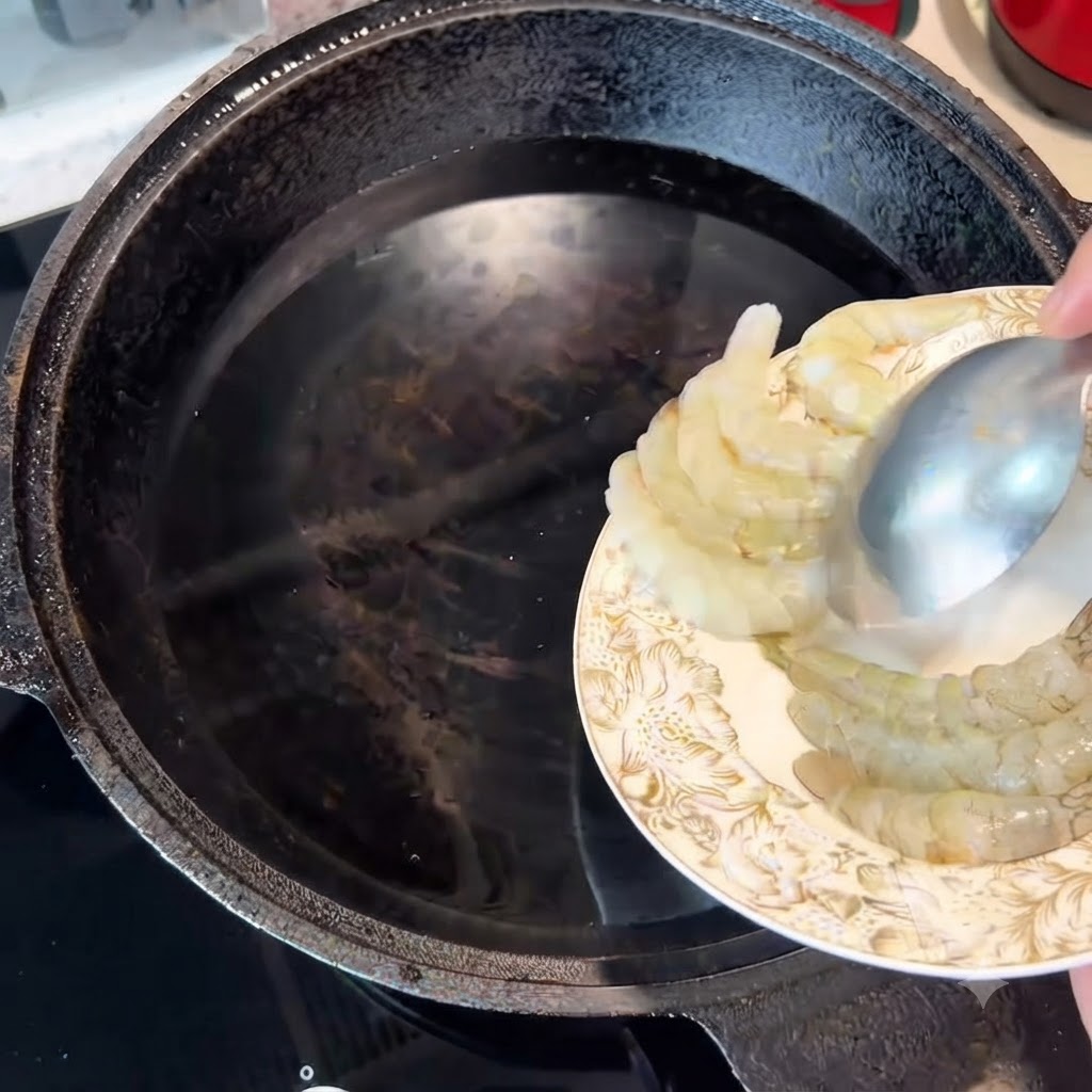 Camarones crudos siendo transferidos con una cuchara a una olla con agua fría.