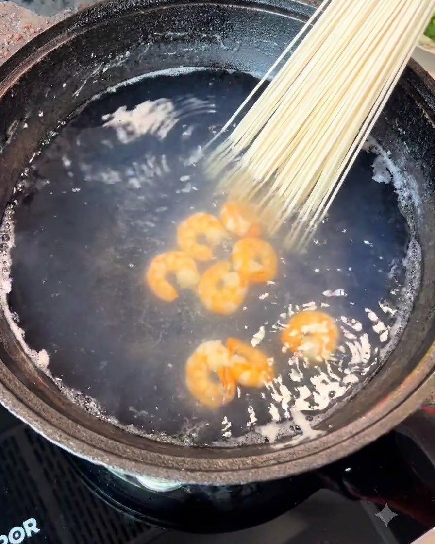 Un manojo de fideos secos siendo colocado en la olla junto con los camarones.