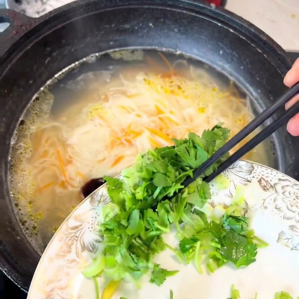 Cilantro y cebollines picados cayendo desde un plato hacia la olla de fideos usando palillos.