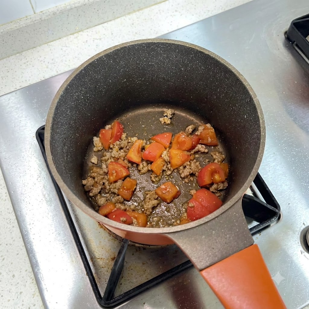 Una olla de cocina llena de una mezcla de ternera picada y tomates en dados siendo sazonada.