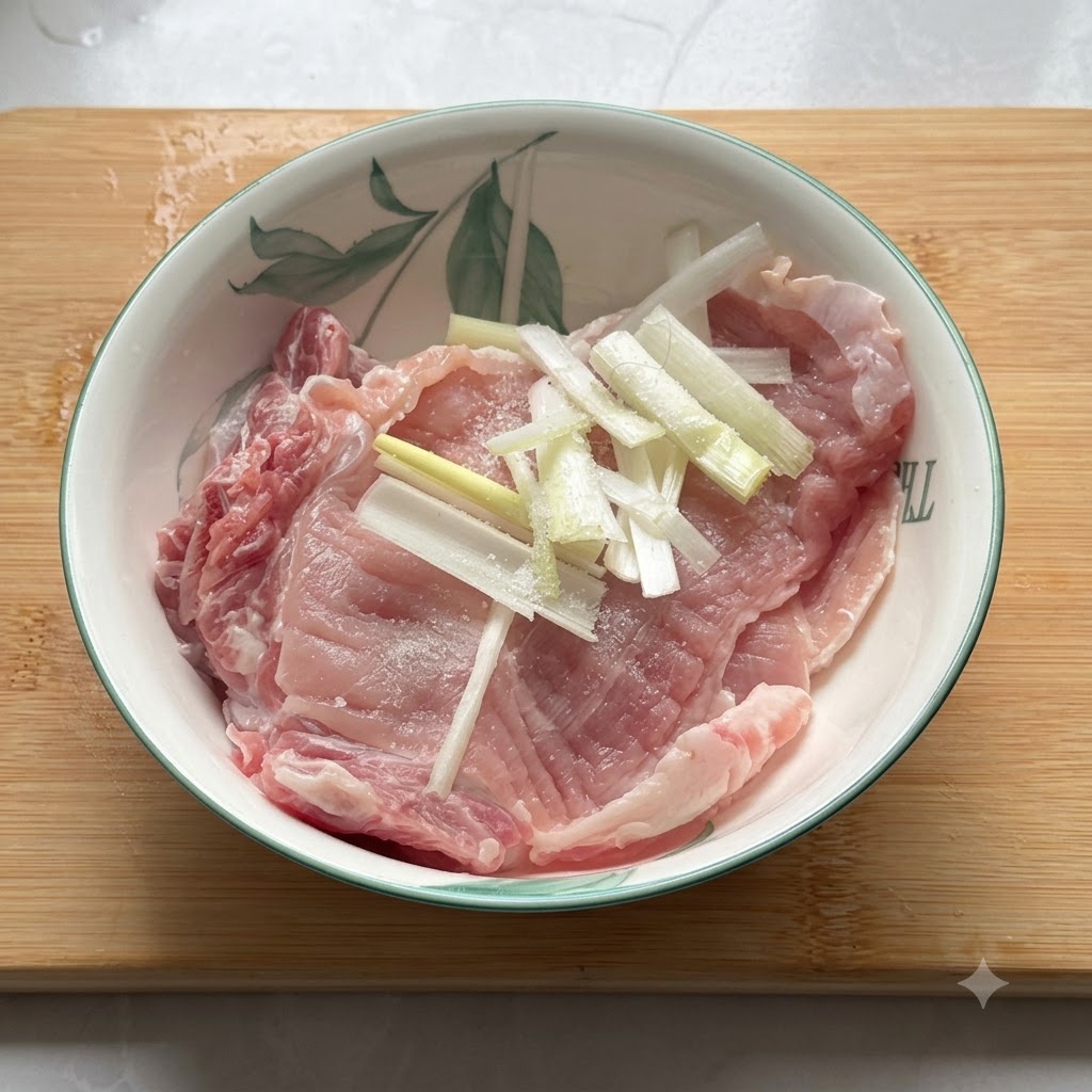 Chuleta de cerdo cruda en un bol de cerámica sazonada con sal, pimienta y trozos de cebollino.